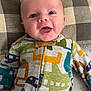 baby, infant, smiling, face, onesie, clothing, pattern, airplane_print, pillow, checkered, fabric, happy, cute, child, person, lying_down, indoors, closeup, portrait, drool
