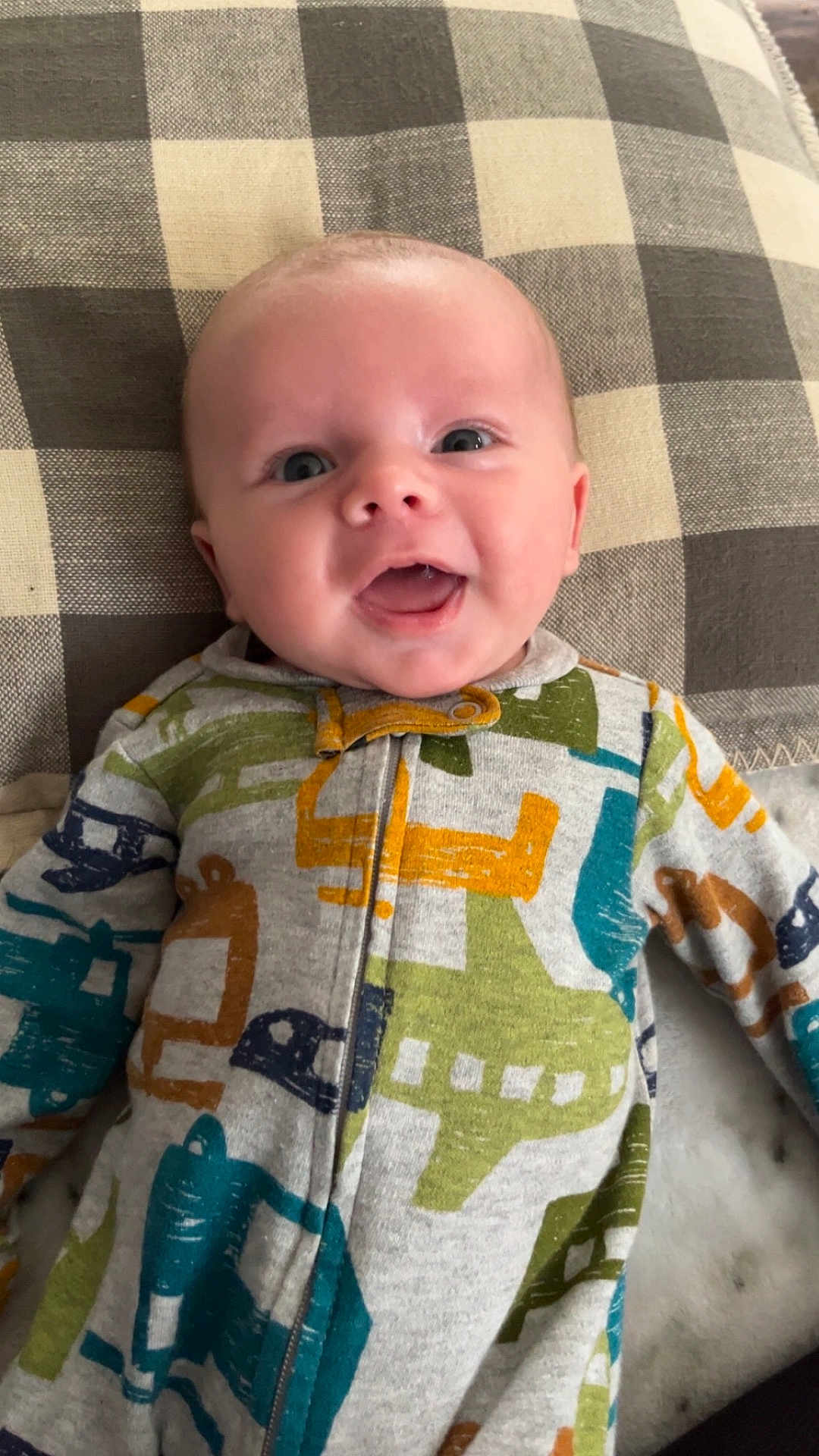 Lennox joined the competition — help win amazing prizes! baby, infant, smiling, face, onesie, clothing, pattern, airplane_print, pillow, checkered, fabric, happy, cute, child, person, lying_down, indoors, closeup, portrait, drool