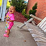 Lauryn is registered to the contest to win money with this photo: toddler, child, smiling, pink_clothing, outdoor, porch, bench, wooden_bench, brick_wall, greenery, plants, concrete, happy, standing, shoes, hair_accessory, daylight, playful, person, casual