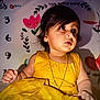 toddler, child, yellow_dress, gold_chain, curly_hair, indoor, portrait, cute, baby, expression, wall_art, flower, numbers, sitting, bright_color, skin, hand, face, young_child, decor