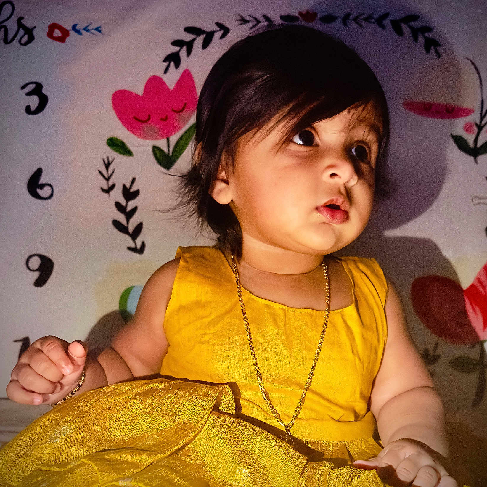 Ayura joined the competition — help win amazing prizes! baby, bright_color, child, curly_hair, cute, decor, expression, face, flower, gold_chain, hand, indoor, numbers, portrait, sitting, skin, toddler, wall_art, yellow_dress, young_child