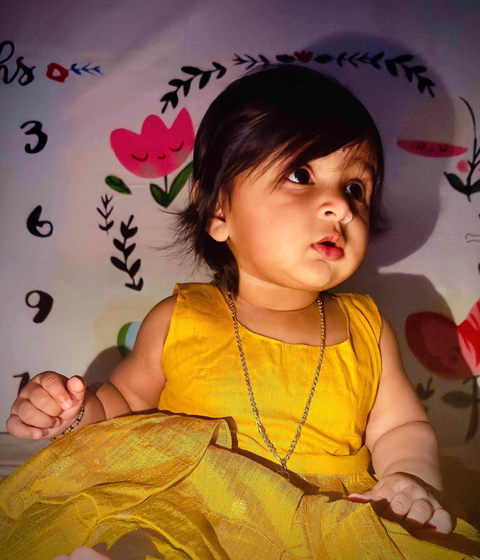 Ayura joined the competition — help win amazing prizes! toddler, child, yellow_dress, gold_chain, curly_hair, indoor, portrait, cute, baby, expression, wall_art, flower, numbers, sitting, bright_color, skin, hand, face, young_child, decor