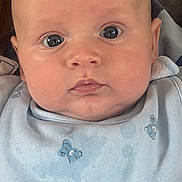 Robin is registered to the contest to win money with this photo: baby, infant, face, blue_bib, teddy_bear_pattern, close_up, wide_eyes, curious, skin, head, child, person, adult_partial_face, soft_lighting, indoor, portrait, cute, small_ears, clothing, neutral_background