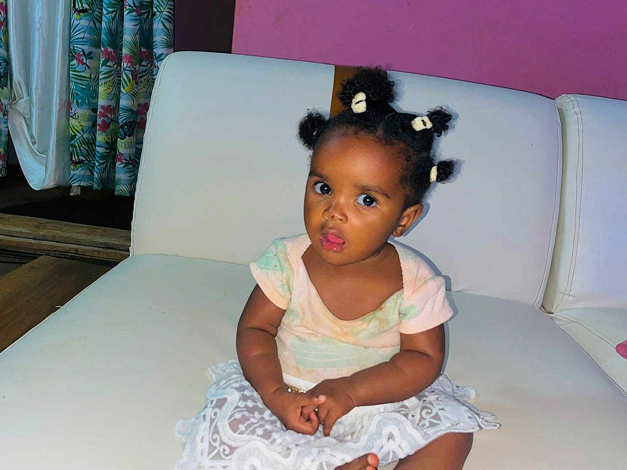 Lumaria Kiazi participe au concours pour gagner de l'argent avec cette photo : baby, child, curly_hair, curtains, cute, expression, face, furniture, hair_puffs, indoor, lace_skirt, pastel_clothing, person, pink_wall, portrait, sitting, toddler, white_couch, wooden_floor, young_child