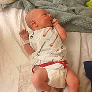 Secil is registered to the contest to win money with this photo: baby, bed, blanket, clothing, cute, diaper, foot, hand, hospital_wristband, indoor, infant, lying_down, newborn, onesie, person, resting, skin, sleepy, soft_fabric, toddler