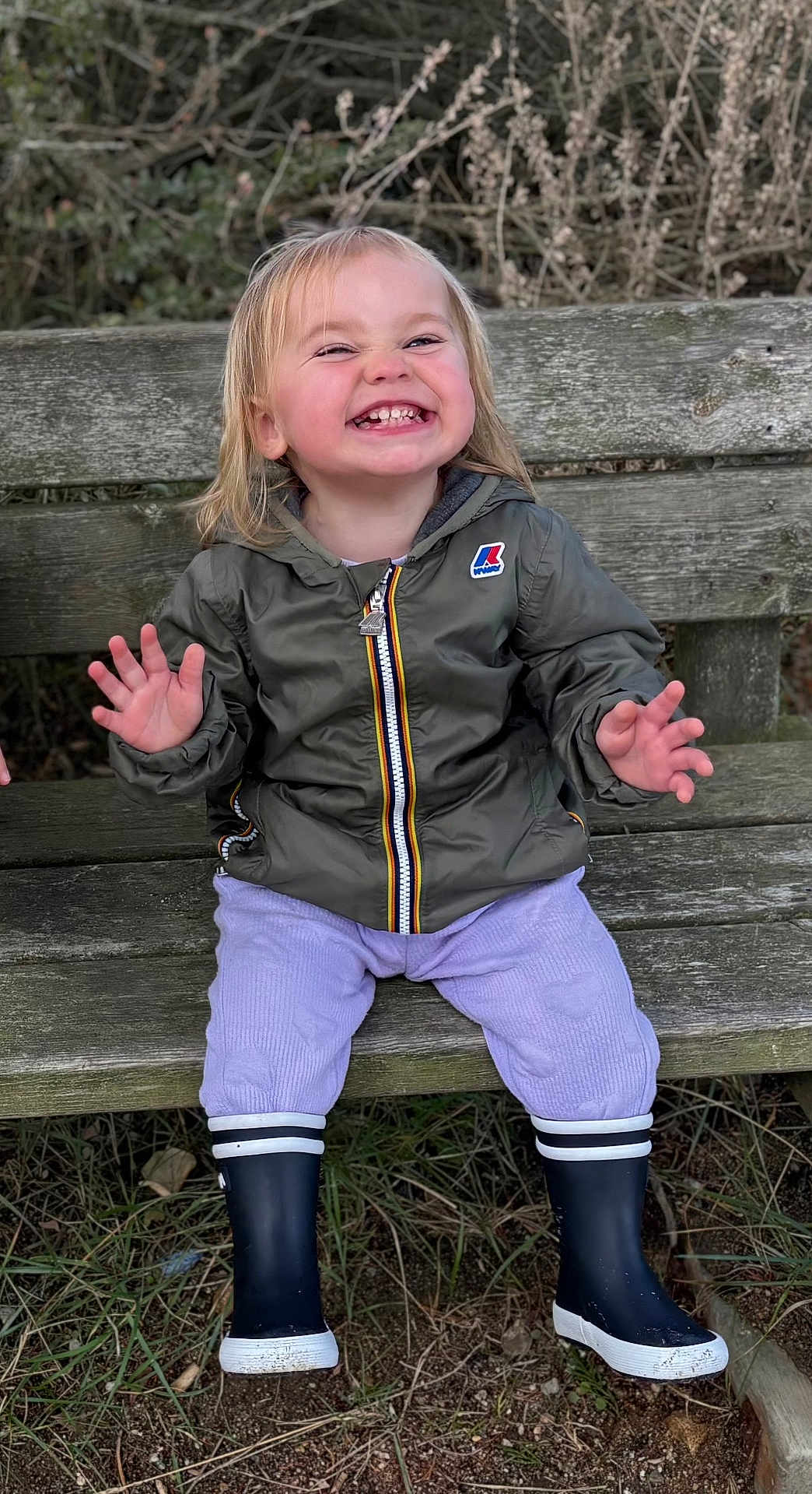 Joséphine a rejoint le concours — aidez-le/la à gagner de superbes lots ! toddler, child, smile, laughing, jacket, boots, bench, outdoor, grass, wood, nature, person, happy, clothing, pants, face, hair, sitting, expression, park