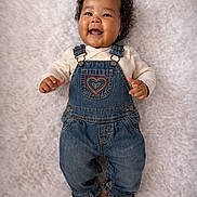 Janiyah is registered to the contest to win money with this photo: baby, infant, smiling, overalls, denim, heart_patch, purple_bow, curly_hair, lying_down, cozy_blanket, portrait, studio_style, happy, cute, toddler_clothes, tiny_shoes, one_piece, closeup, adorable, child