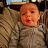 Sonny is registered to the contest to win money with this photo: baby, infant, child, portrait, close_up, face, eyes, wide_eyed, indoors, blanket, onesie, clothing, sitting, lying_down, cozy, home, furniture, television, window, smiling