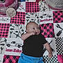 baby, infant, child, black_shirt, blue_pants, patchwork_quilt, tools_pattern, truck_pattern, lying_down, curious_expression, indoor, fabric, colorful, cute, young_child, portrait, clothing, person, floor, soft_texture