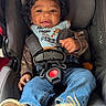 Kaison is registered to the contest to win money with this photo: toddler, child, car_seat, smiling, curly_hair, denim_jeans, bib, shoes, sole, seatbelt, happy, indoor, clothing, baby, person, cute, infant, seat, car_accessory, portrait
