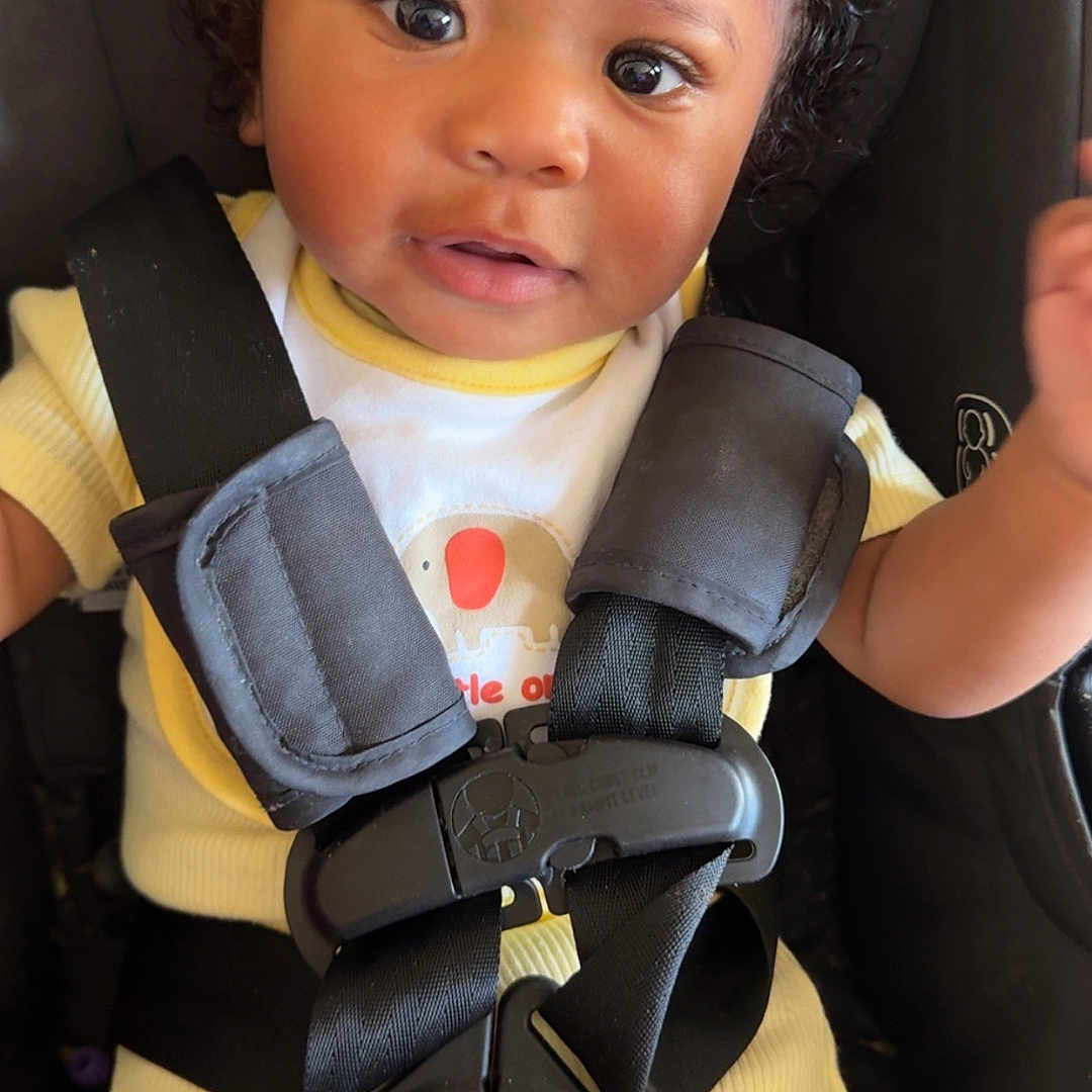 Kaison joined the competition — help win amazing prizes! baby, child, car_seat, curly_hair, yellow_outfit, straps, safety_harness, infant, cute, smiling, portrait, seat, seatbelt, young_child, indoor, person, looking_at_camera, happy, skin, face