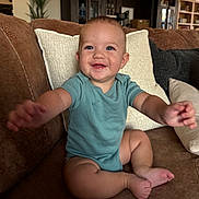 Jesse joined the competition — help win amazing prizes! baby, child, smiling, happy, couch, living_room, onesie, arm, foot, pillow, furniture, indoor, person, face, blue_eyes, skin, home, cute, seated, infant