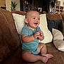 Jesse is registered to the contest to win money with this photo: baby, smiling, clapping, onesie, couch, pillow, indoor, child, infant, happy, person, home, furniture, living_room, cute, seated, skin, foot, hand, face