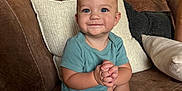 Jesse is registered to the contest to win money with this photo: baby, child, blue_eyes, smiling, sitting, cross_legged, hands_clasped, brown_couch, leather_couch, pillows, indoor, living_room, furniture, cabinet, plant, homedecor, cute, infant, portrait, happy