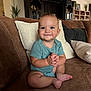 baby, child, blue_eyes, smiling, sitting, cross_legged, hands_clasped, brown_couch, leather_couch, pillows, indoor, living_room, furniture, cabinet, plant, homedecor, cute, infant, portrait, happy