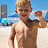 child, boy, beach, seaside, summer, smiling, portrait, wet_hair, sunlight, sand, swim_trunks, colorful_clothing, water_drops, snack, food, seagull, umbrellas, blue_sky, outdoor, vacation