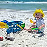 Dawson is registered to the contest to win money with this photo: child, toddler, beach, sand, ocean, seaside, yellow_hat, swimsuit, shovel, bucket, sand_toys, smiling, sitting, outdoor, summer, sunny, shoreline, waves, colorful_toys, portrait