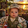 baby, child, hat, vest, fishing_rod, plush_toy, blanket, lake, sunset, outdoor, nature, bucket, lantern, wooden_sign, fishing_net, water, trees, sky, cute, portrait