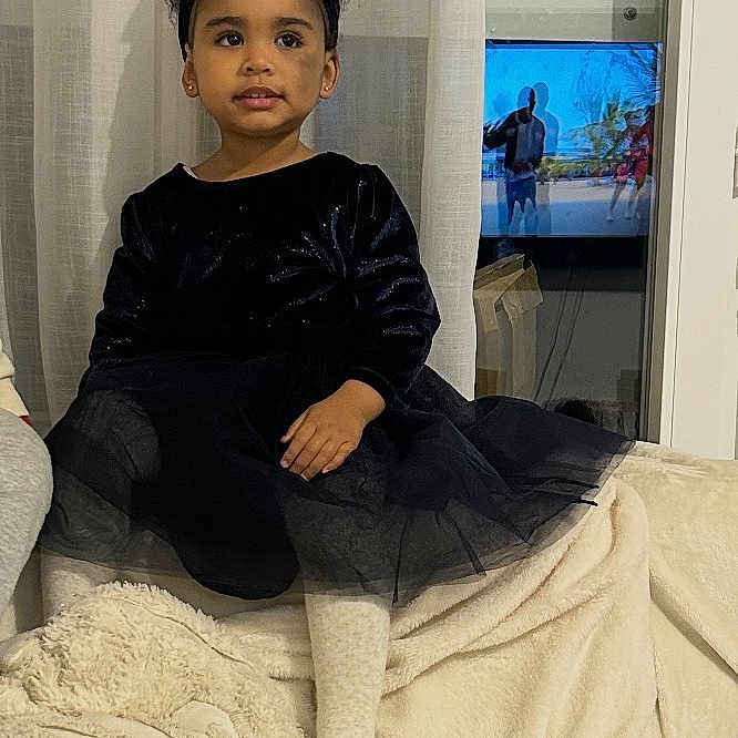 Djennah a rejoint le concours — aidez-le/la à gagner de superbes lots ! black_dress, blanket, child, couch, cozy, curtain, curtains, furniture, girl, headband, home, indoors, living_room, person, portrait, screen, sitting, smiling, television, window