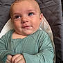 baby, infant, child, face, smile, blue_eyes, green_clothing, hands, quilted_background, seat, cushion, portrait, closeup, cute, young, cozy, indoors, apparel, person, expression