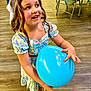 child, girl, balloon, blue_balloon, smiling, happy, dress, floral_dress, indoor, flooring, wood_floor, chair, table, party, celebration, person, long_hair, curly_hair, playful, joyful