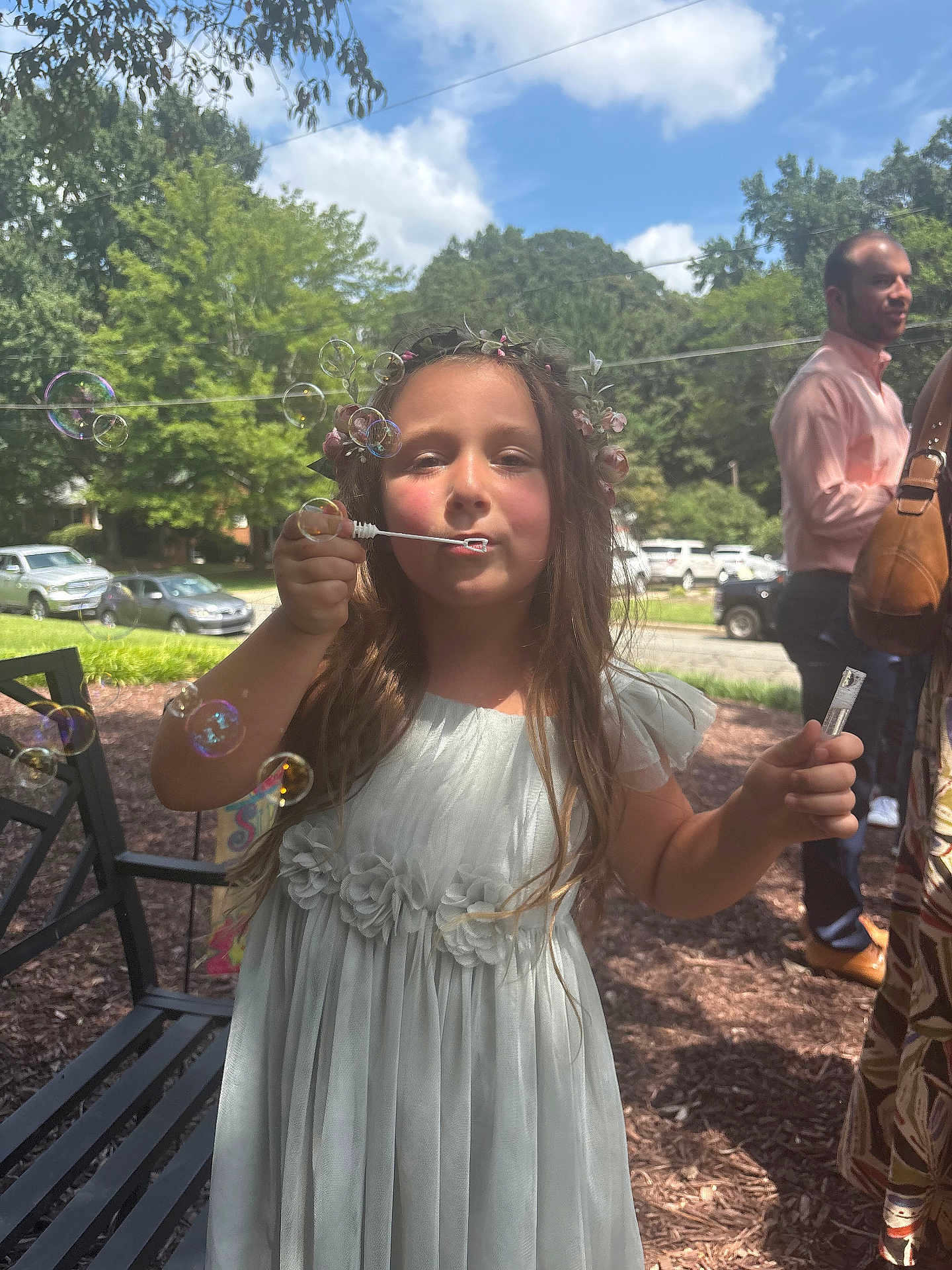 Rosemary is registered to the contest to win money with this photo: child, girl, bubble, outdoor, dress, flower_crown, sunlight, nature, tree, bench, people, grass, car, celebration, happy, play, summer, portrait, casual, fun
