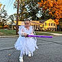 Rosemary is registered to the contest to win money with this photo: child, girl, white_dress, toy_sword, purple_sword, outdoor, street, autumn, fall, trees, house, suburb, smiling, posing, costume, playful, sunlight, sneakers, sidewalk, daytime