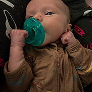Colson joined the competition — help win amazing prizes! baby, infant, pacifier, onesie, close_up, portrait, hand, fist, awake, newborn, brown_clothing, zipper, face, mouth, eyes, blanket, patterned_clothing, parent_lap, indoor, cute