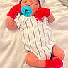 baby, newborn, pacifier, hat, mittens, socks, onesie, striped_clothing, red_color, white_blanket, sleeping, infant, cute, soft_texture, lying_down, cozy, small_person, child, indoor, portrait