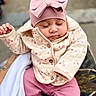 baby, child, sleeping, pink_bow, hat, jacket, floral_pattern, pink_pants, outdoor, person, cute, warm_clothing, hand, holding, peaceful, portrait, infant, soft_texture, cozy, closeup