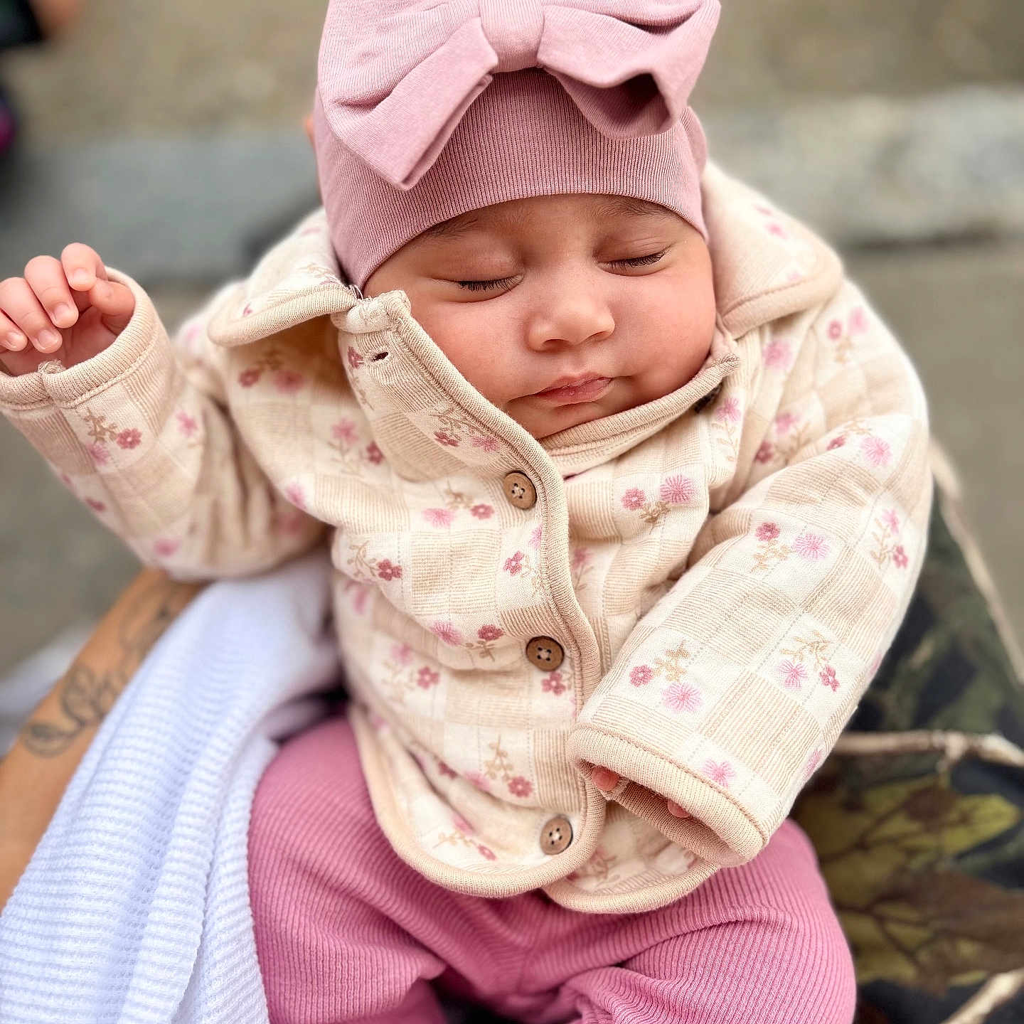 Sophia is registered to the contest to win money with this photo: baby, child, sleeping, pink_bow, hat, jacket, floral_pattern, pink_pants, outdoor, person, cute, warm_clothing, hand, holding, peaceful, portrait, infant, soft_texture, cozy, closeup