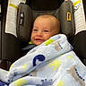 baby, blanket, car_seat, child, cozy, eyes, fabric, face, happy, head, indoors, infant, portrait, safety_labels, sitting, smiling, text, travel, vehicle, wrapped