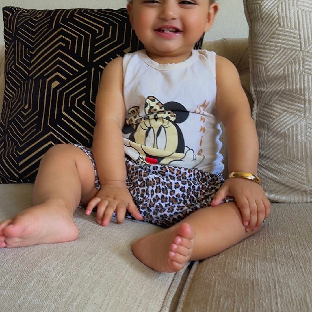 Khadijah joined the competition — help win amazing prizes! toddler, child, smiling, sitting, couch, indoor, face, happy, clothing, tank_top, shorts, patterned_cushion, hair_ties, barefoot, skin, person, cute, playful, leopard_print, minnie_mouse