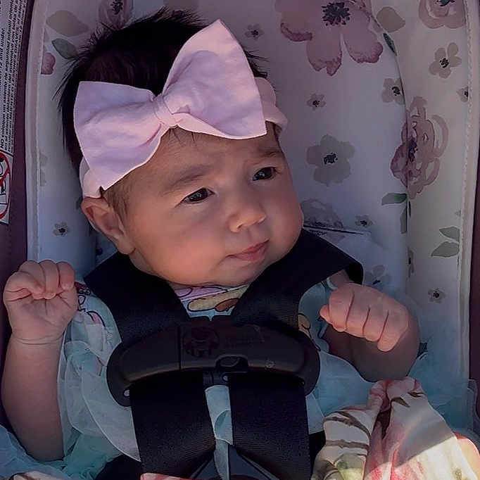 Kaylani joined the competition — help win amazing prizes! baby, infant, car_seat, pink_bow, headband, blanket, floral_pattern, clothing, cute, child, small_hands, face, portrait, sitting, indoors, safety_harness, young_child, expression, soft_light, close_up