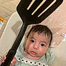 Kaylani is registered to the contest to win money with this photo: baby, child, closeup, cute, daisies, expression, eyes, fabric, face, green_clothing, hand, holding, indoor, infant, kitchen_utensil, pattern, person, portrait, spatula, texture