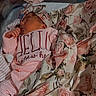 newborn, baby, sleeping, blanket, floral_pattern, headband, hospital_bassinet, pink_clothing, infant, peaceful, portrait, child, cute, resting, soft_lighting, indoors, baby_clothes, announcement_sign, cozy, wrapped
