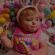 Nova is registered to the contest to win money with this photo: baby, child, bunny_ears, pink_bib, snack, easter_eggs, colorful, cute, tutu, sitting, indoor, playful, holiday_theme, face, expression, young_child, festive, soft_lighting, portrait, holding