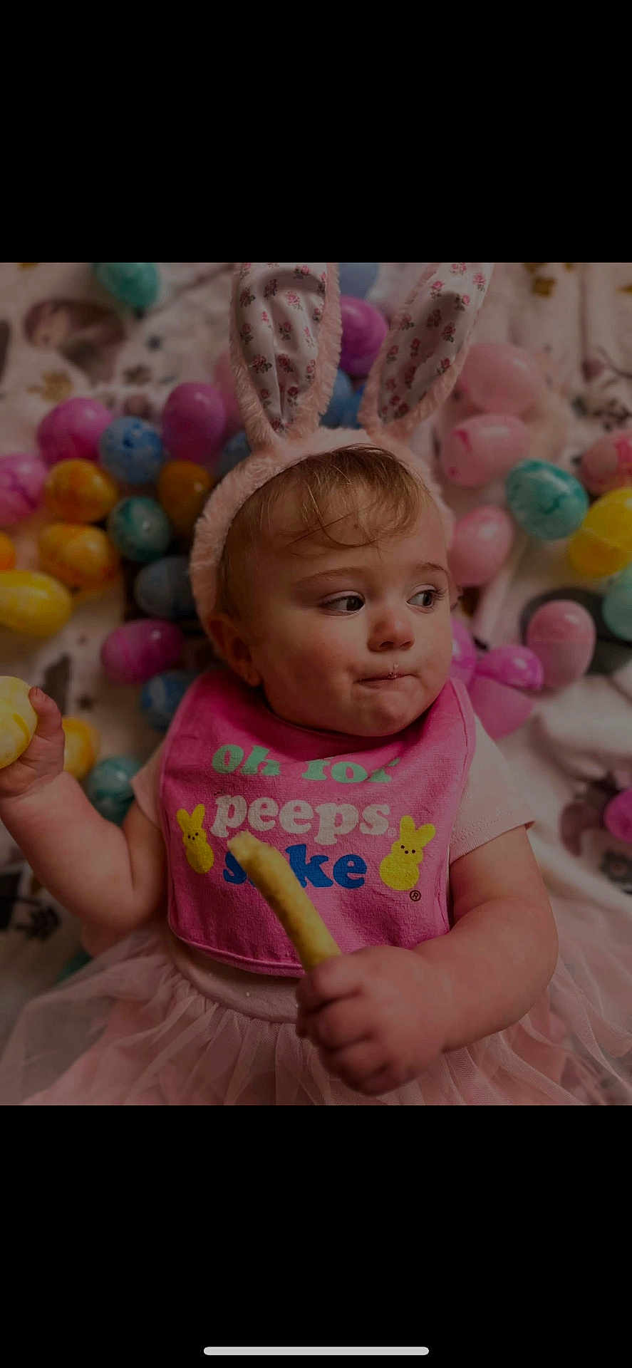 Nova is registered to the contest to win money with this photo: baby, child, bunny_ears, pink_bib, snack, easter_eggs, colorful, cute, tutu, sitting, indoor, playful, holiday_theme, face, expression, young_child, festive, soft_lighting, portrait, holding