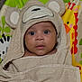 baby, child, towel, hood, bear, animal_print, cushion, colorful, face, eyes, cute, infant, wrapped, curious, expression, indoors, soft, texture, portrait, young
