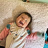 baby, smiling, lying_down, blanket, onesie, happy, infant, child, cute, soft_texture, waving_hand, indoors, face, clothing, head, person, joyful, playful, cozy, expression