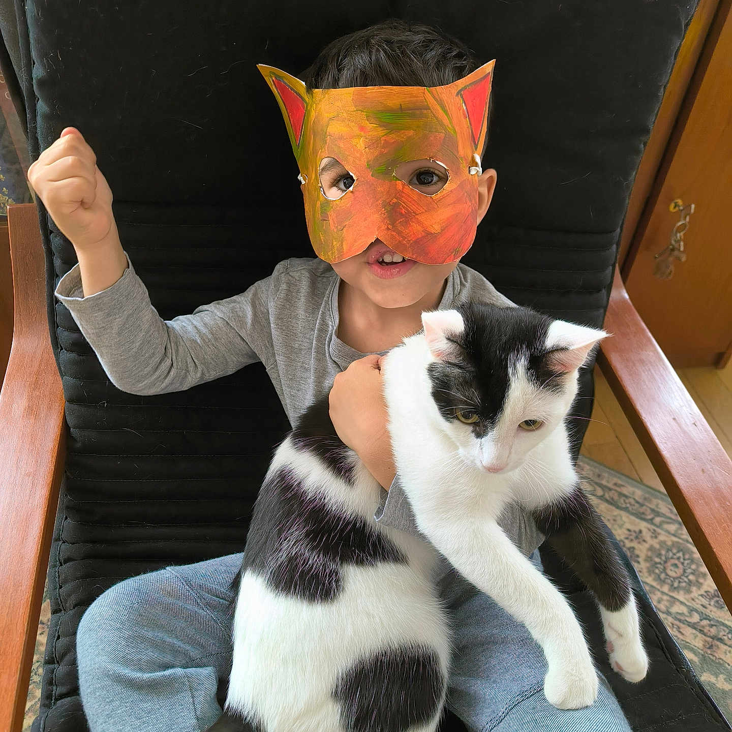 Tony participe au concours pour gagner de l'argent avec cette photo : animal, black_and_white_cat, carpet, cat_mask, chair, child, cushion, cute, face_mask, gray_clothing, happy, holding, home, indoor, pet, playful, raised_fist, sitting, wooden_armrest, young_child