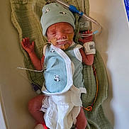 Rohan is registered to the contest to win money with this photo: newborn, baby, infant, medical_tubes, hospital, hat, vest, diaper, green_cloth, monitoring_device, sleeping, fragile, healthcare, tiny, panda_print, skin, lying_down, hands_up, foot_sensor, care
