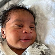 Amir is registered to the contest to win money with this photo: baby, smiling, face, curly_hair, infant, closeup, blanket, white, cozy, cute, newborn, child, portrait, sleepwear, lying_down, soft, skin, happy, indoors, person