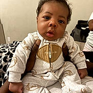 Da'Choice joined the competition — help win amazing prizes! baby, child, infant, portrait, sitting, face, curious, indoor, onesie, jumpsuit, football_pattern, carrier, clothing, adult, bedroom, blanket, furniture, cozy, photography, closeup