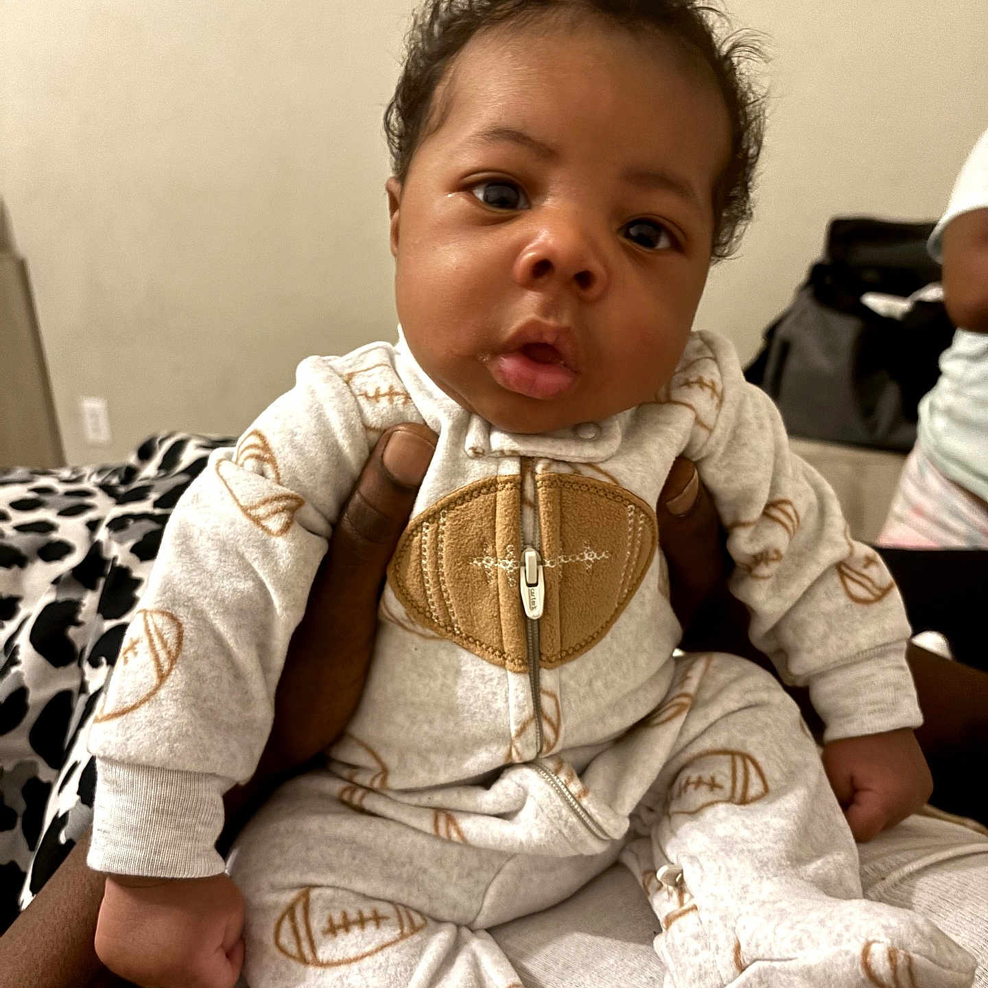 Da'Choice joined the competition — help win amazing prizes! baby, child, infant, portrait, sitting, face, curious, indoor, onesie, jumpsuit, football_pattern, carrier, clothing, adult, bedroom, blanket, furniture, cozy, photography, closeup