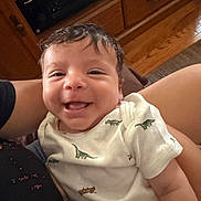 Ibrahim joined the competition — help win amazing prizes! baby, smiling, infant, dinosaur_print, onesie, person, indoor, wooden_cabinet, floor, happy, portrait, child, cute, toddler, holding, hair, face, casual, candid, comfort