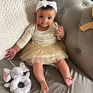 Talia joined the competition — help win amazing prizes! baby, child, headband, bow, dress, tulle_skirt, couch, plush_toy, elephant, knit_blanket, infant, smiling, indoor, cute, person, fabric, foot, hand, seated, home