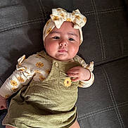 Jailani is registered to the contest to win money with this photo: baby, child, infant, portrait, lying_down, indoors, headband, bow, floral_pattern, sunflowers, overalls, dress, cushion, sofa, textile, smiling, face, hands, fashion, photography