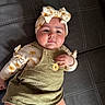 baby, child, infant, portrait, lying_down, indoors, headband, bow, floral_pattern, sunflowers, overalls, dress, cushion, sofa, textile, smiling, face, hands, fashion, photography