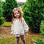 blonde, brownhair, child, clothing, conifer, face, female, girl, hair, happy, head, knitwear, person, plant, sitting, sleeve, smile, standing, sweater, tree